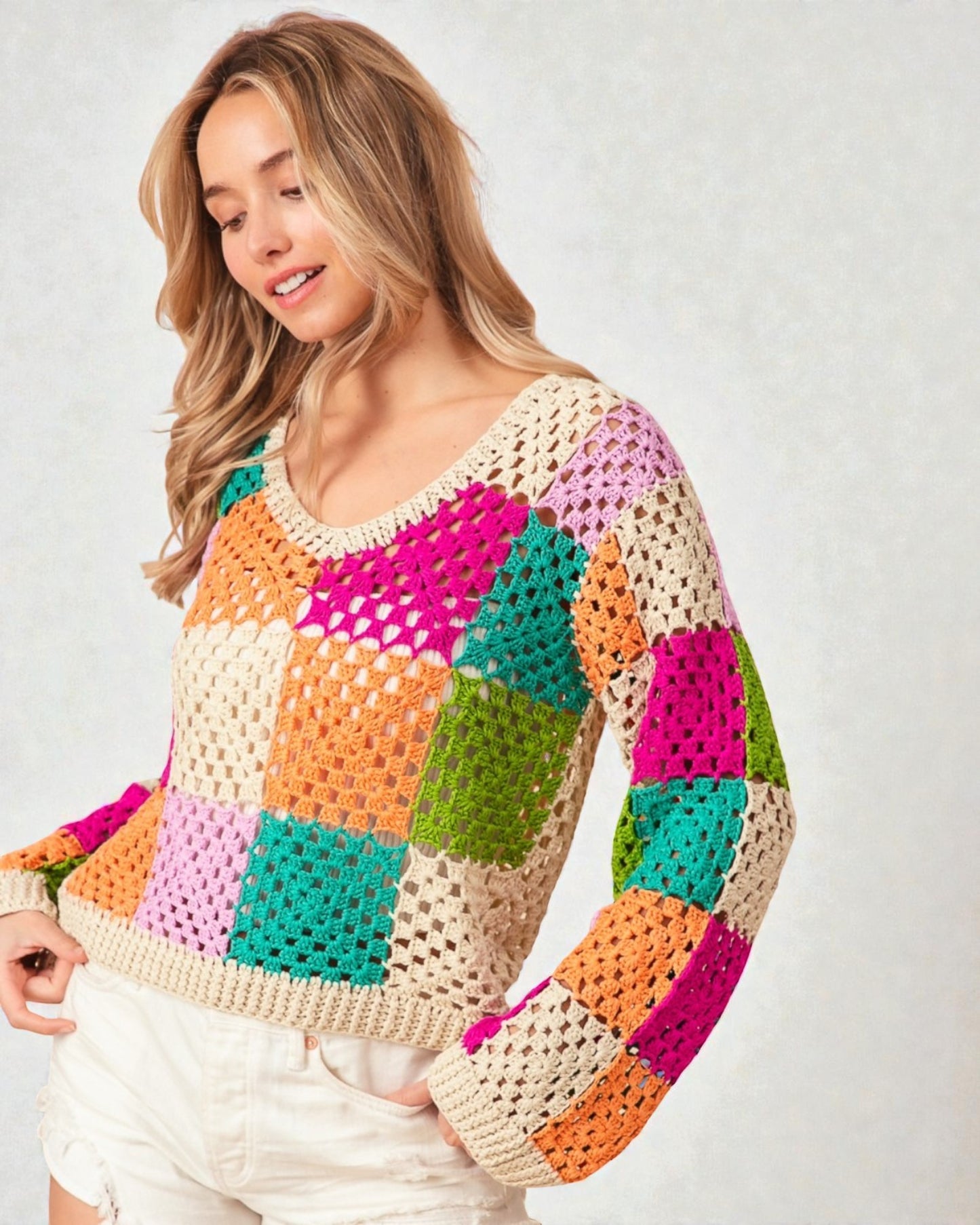Woman wearing a colorful crochet sweater on a plain background