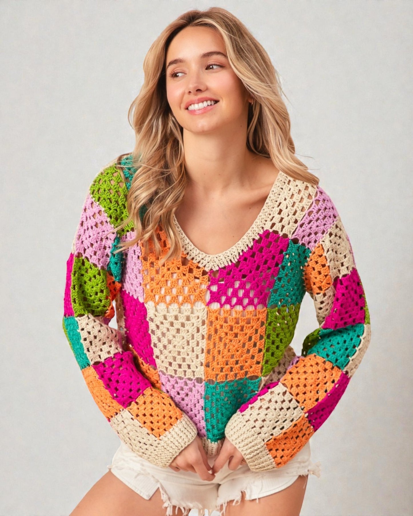 Woman wearing a colorful crochet sweater on a plain background