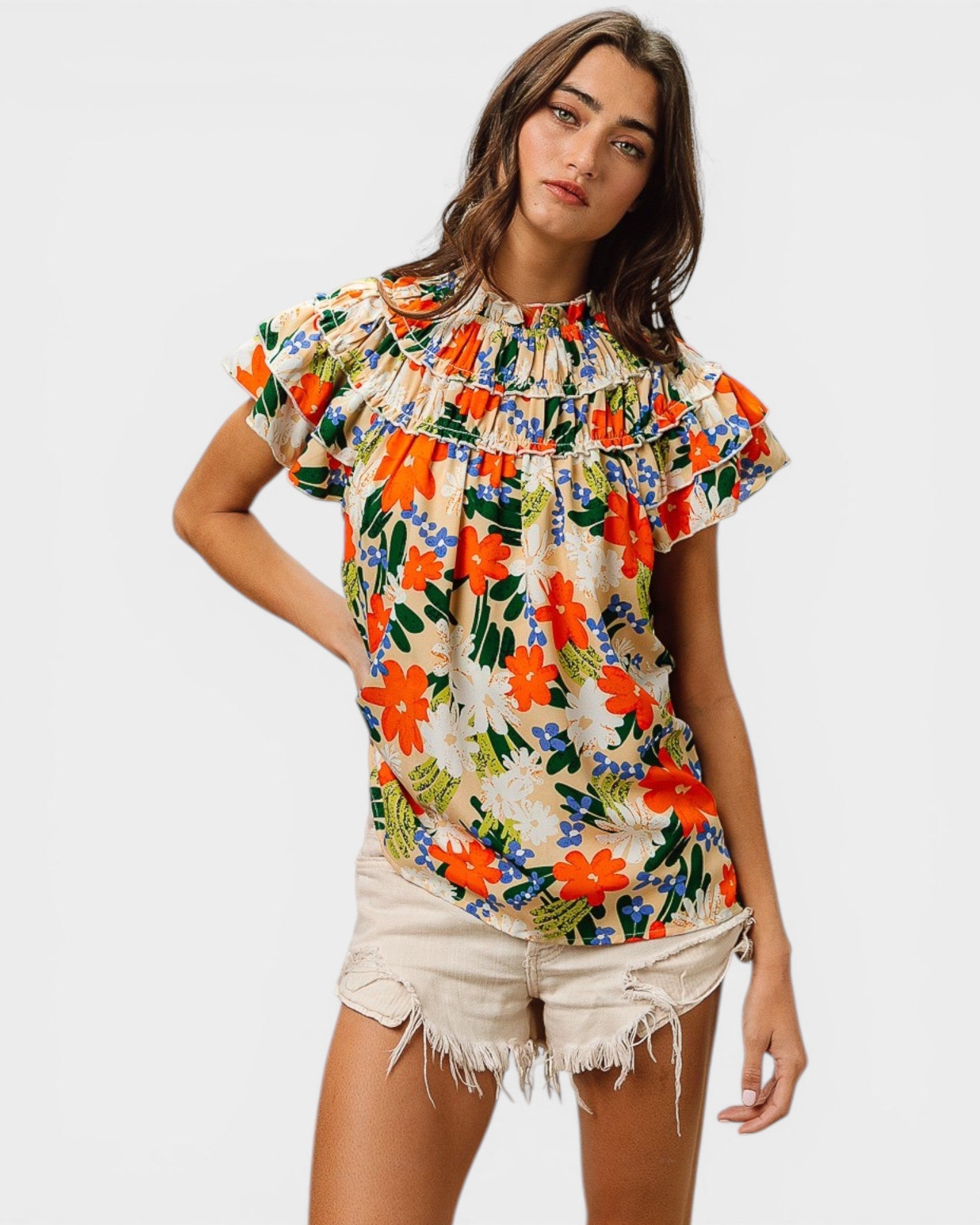 Woman wearing a colorful floral blouse with white shorts on a light gray background