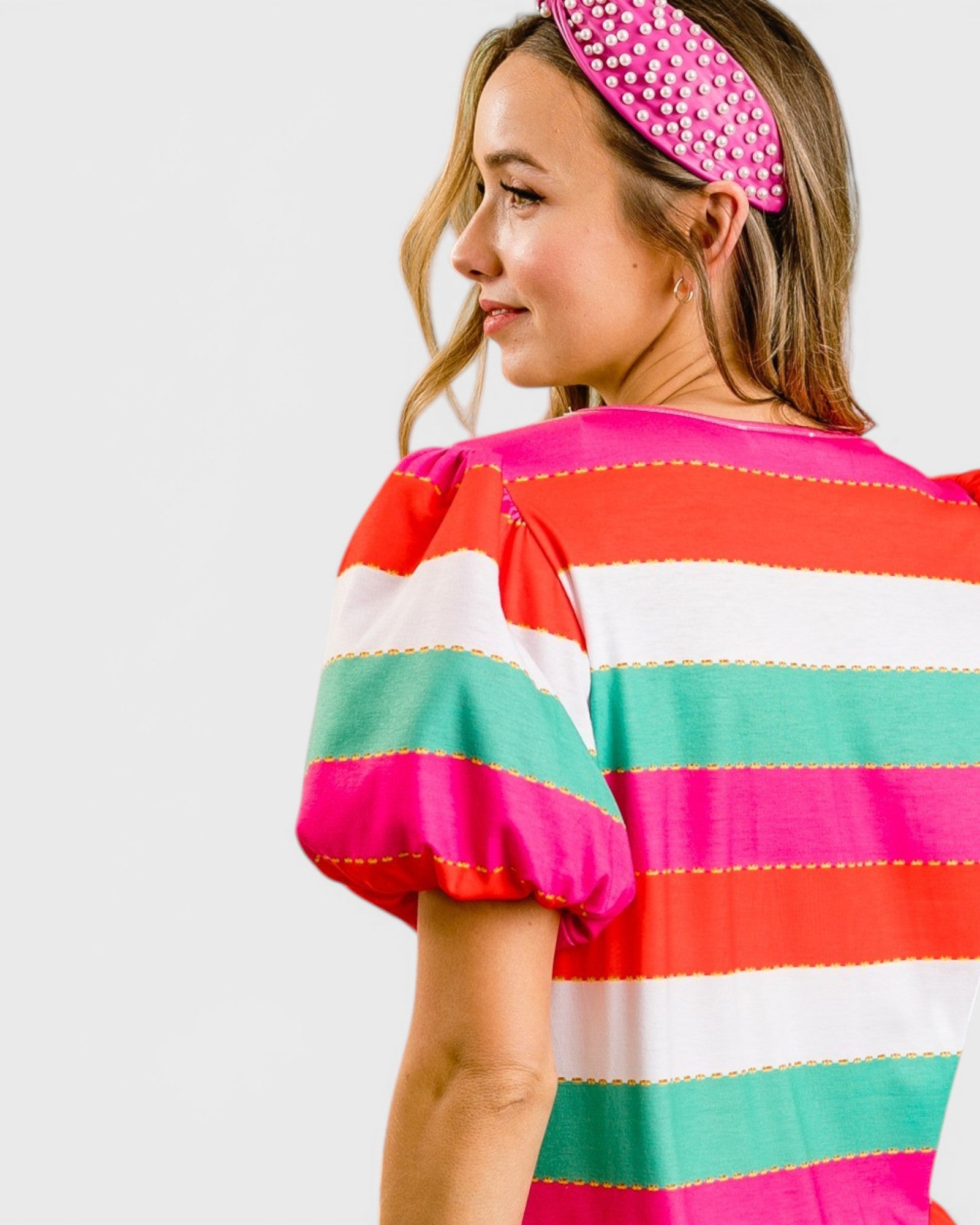 Woman wearing a colorful striped dress with a pink headband on a white background