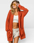 Woman wearing a rust-colored cardigan over a white top and light shorts, with yellow sunglasses on a white background.
