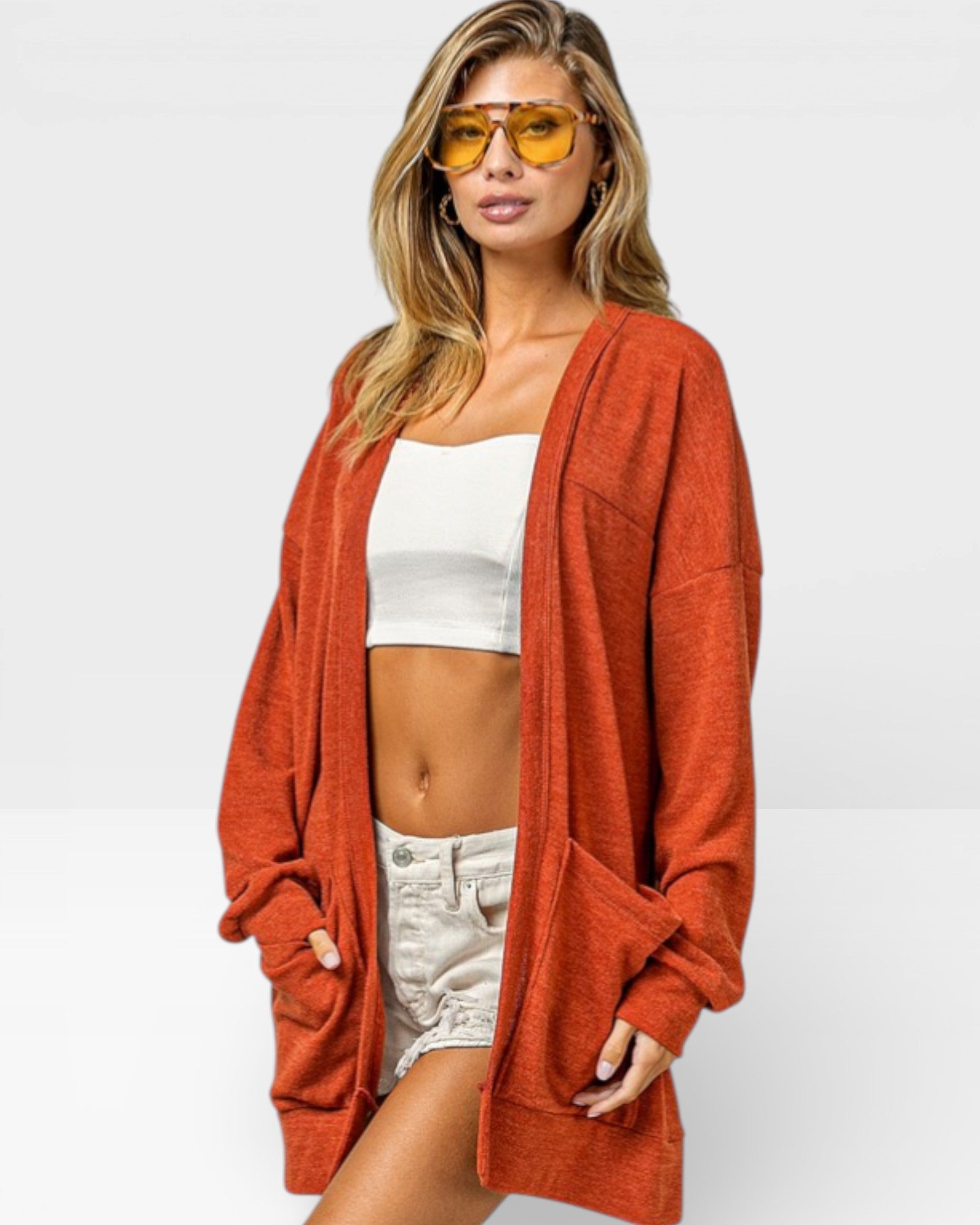 Woman wearing a rust-colored cardigan over a white top and shorts on a light gray background