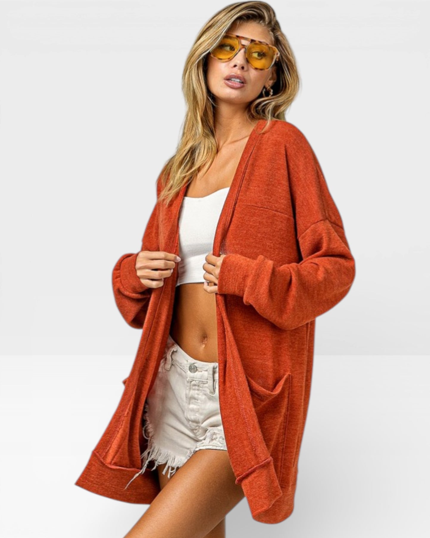 Woman wearing a rust-colored cardigan over a white top and denim shorts on a white background