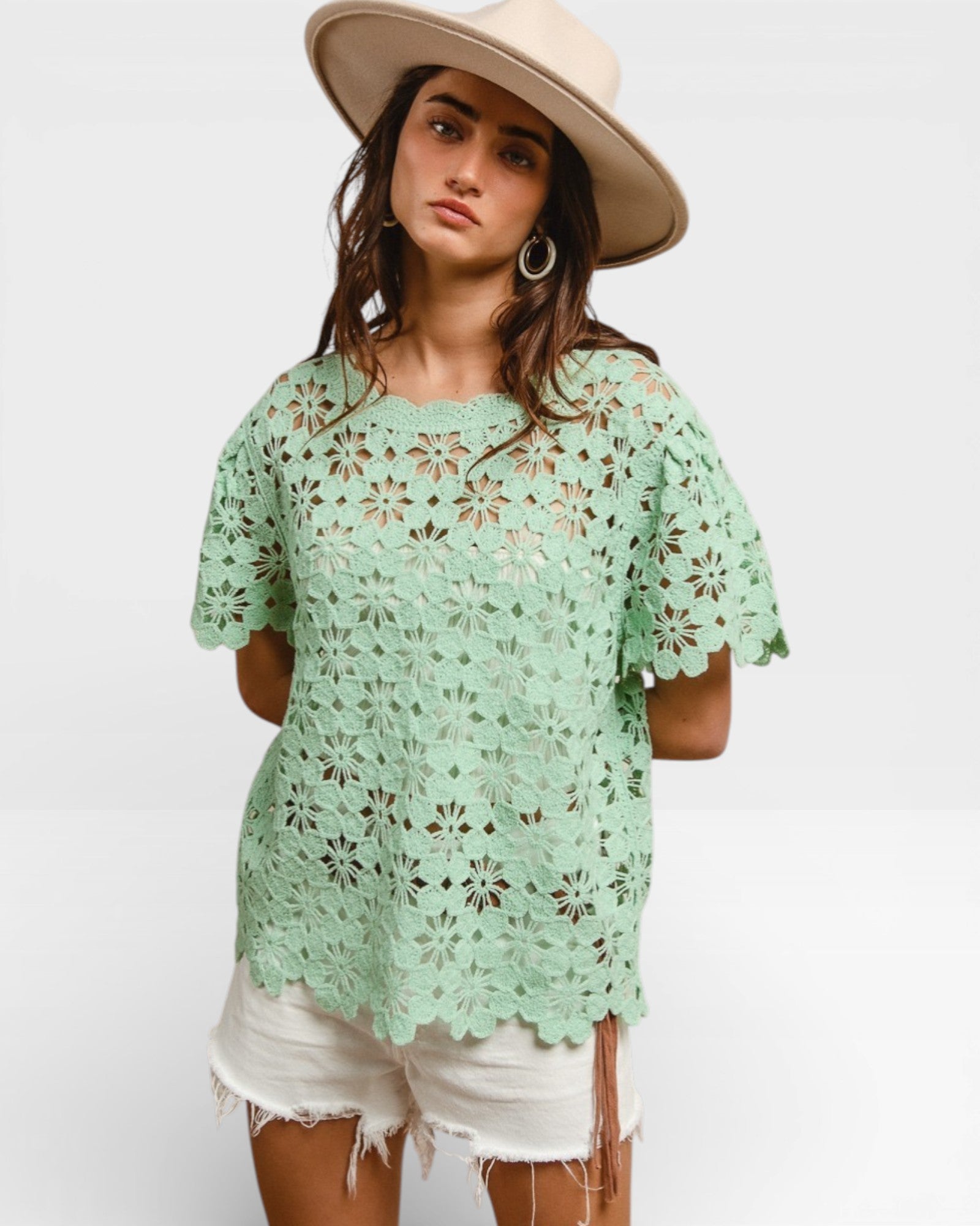 Woman wearing a light green crochet top and beige hat on a white background