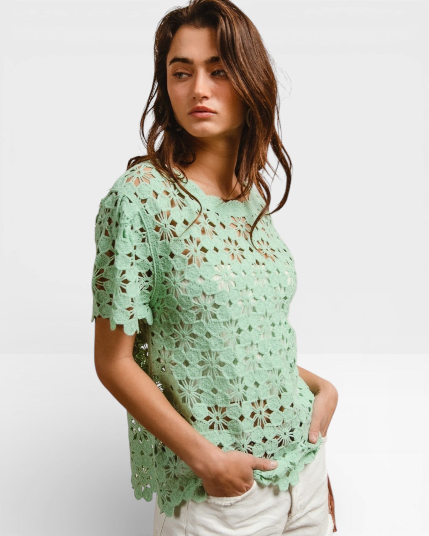 Woman wearing a light green crochet top against a white background