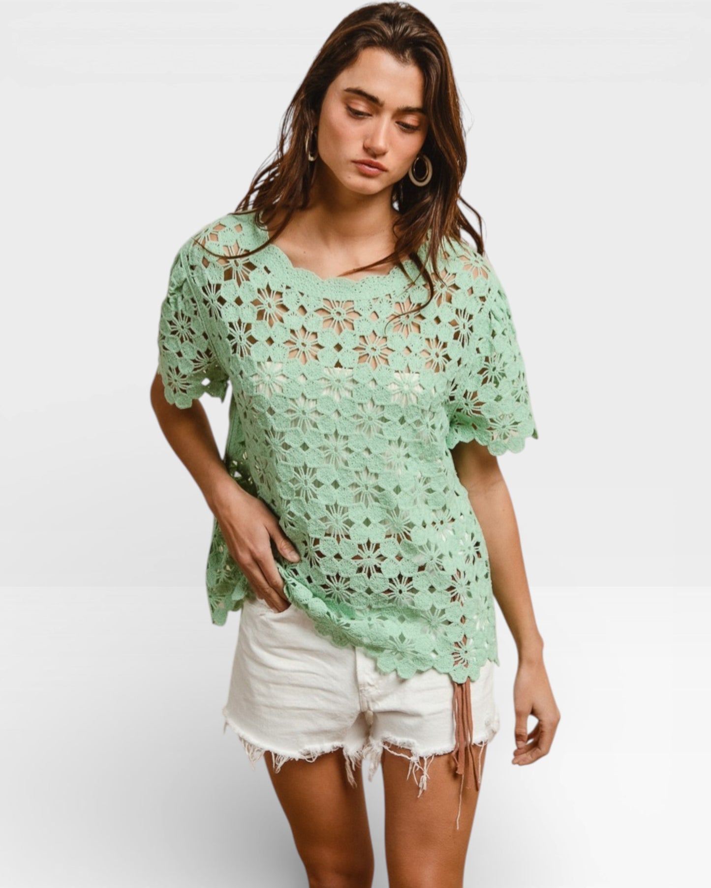 Woman wearing a light green crochet top and white shorts on a white background