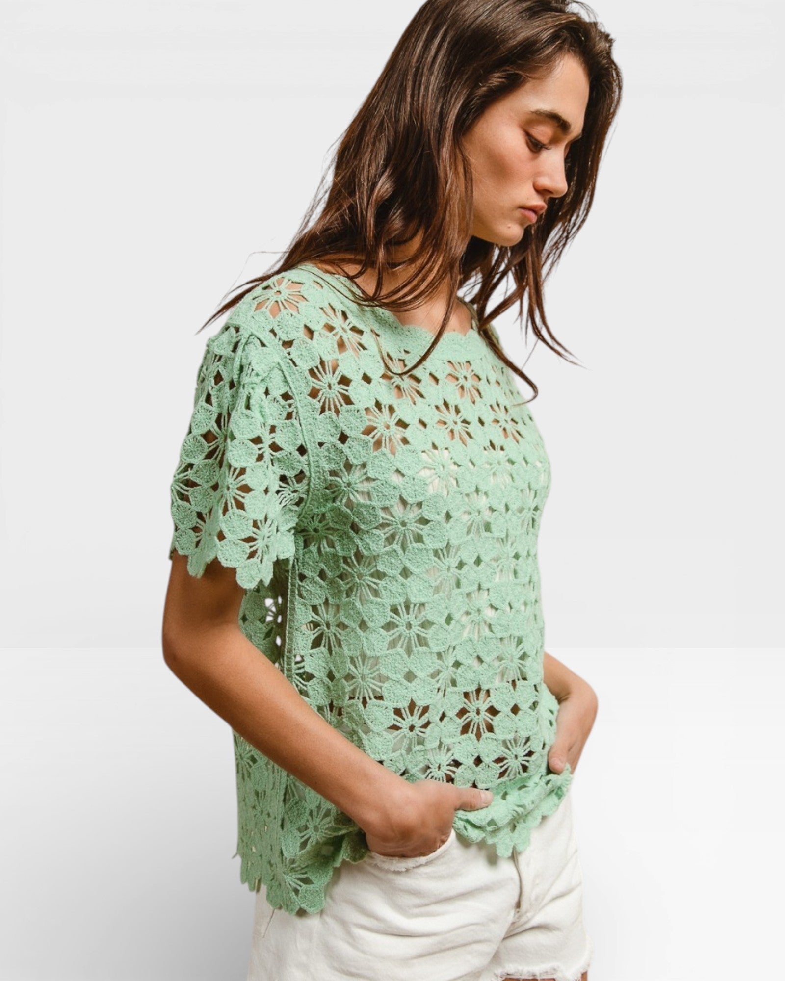 Woman wearing a light green crochet top against a white background