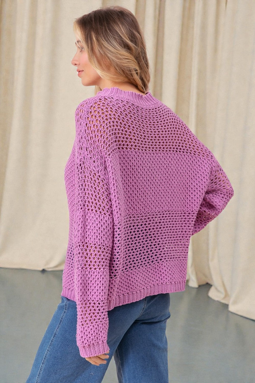 Woman wearing a purple knitted sweater and blue jeans against a neutral background