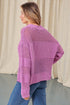 Woman wearing a purple knitted sweater and blue jeans against a neutral background