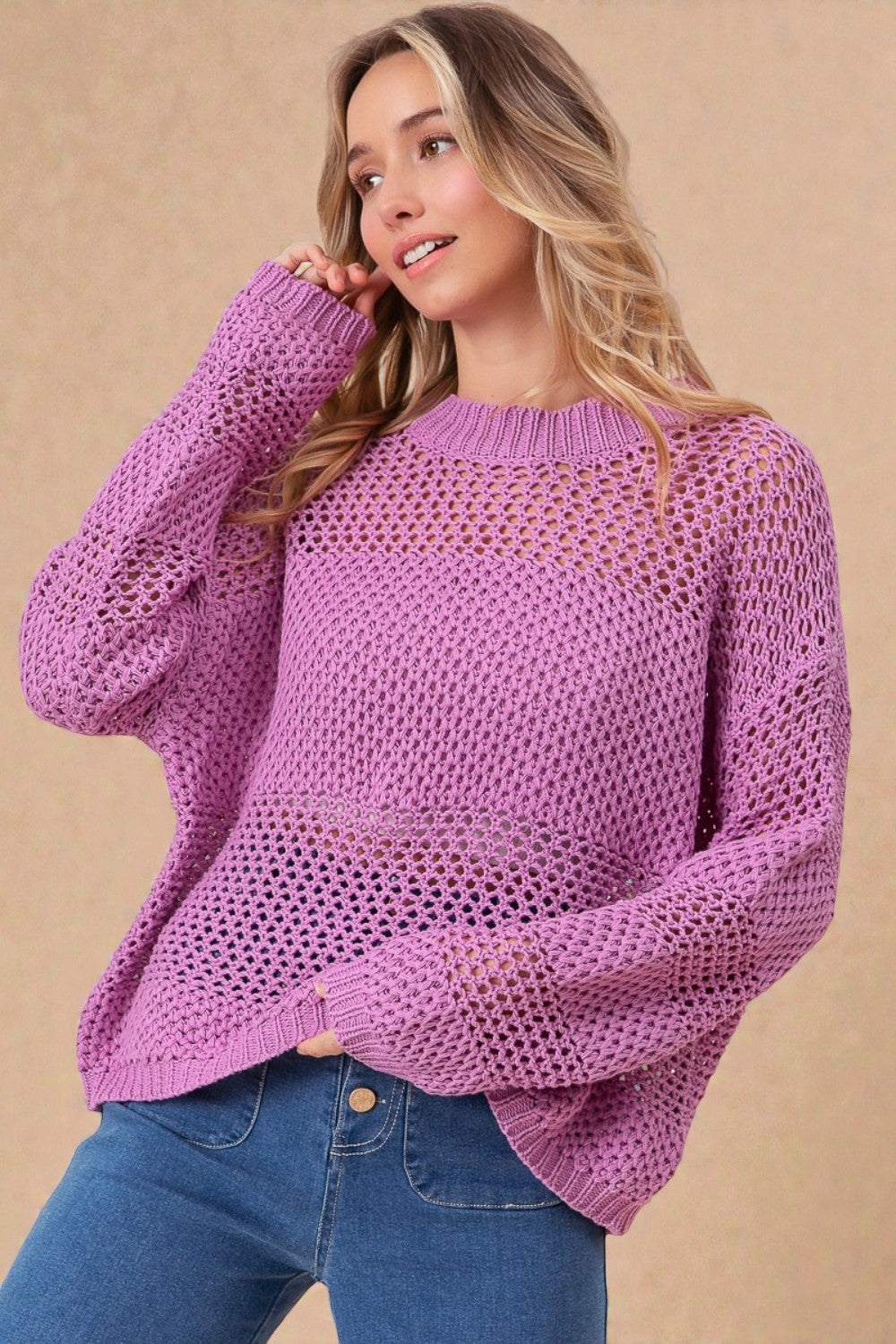 Woman wearing a purple sweater and blue jeans against a beige background