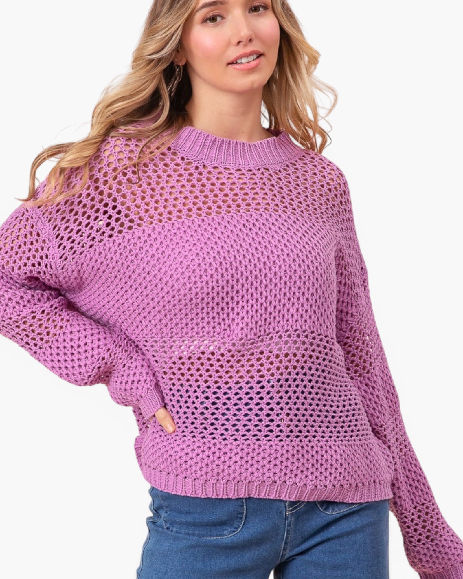 A woman wearing a lavender open-knit crewneck sweater and blue jeans, photographed against a plain light background.