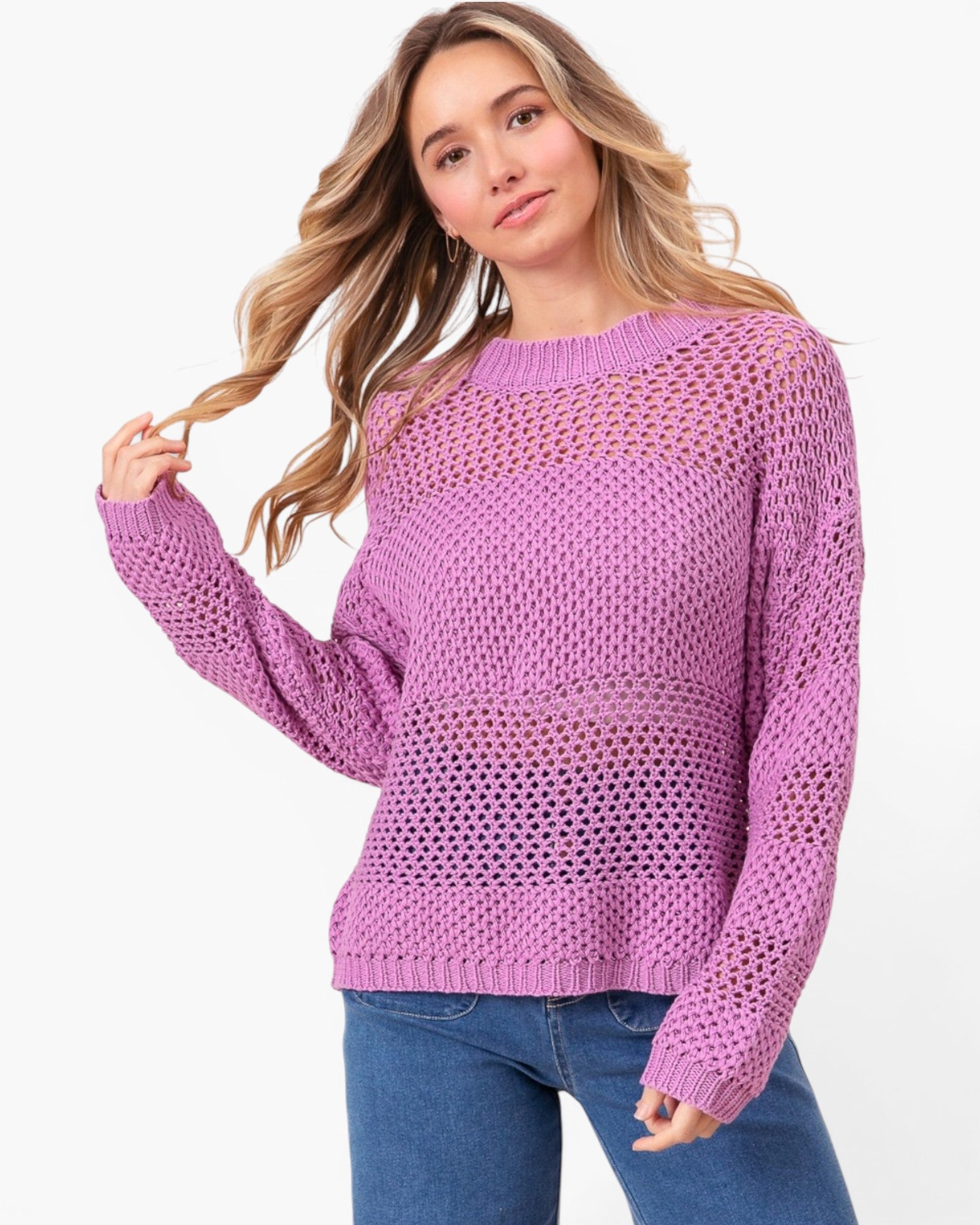 A woman wearing a lavender open-knit crewneck sweater and blue jeans, posing against a solid white studio background.