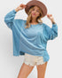 Woman wearing a blue oversized sweatshirt and white shorts with a brown hat on a plain background