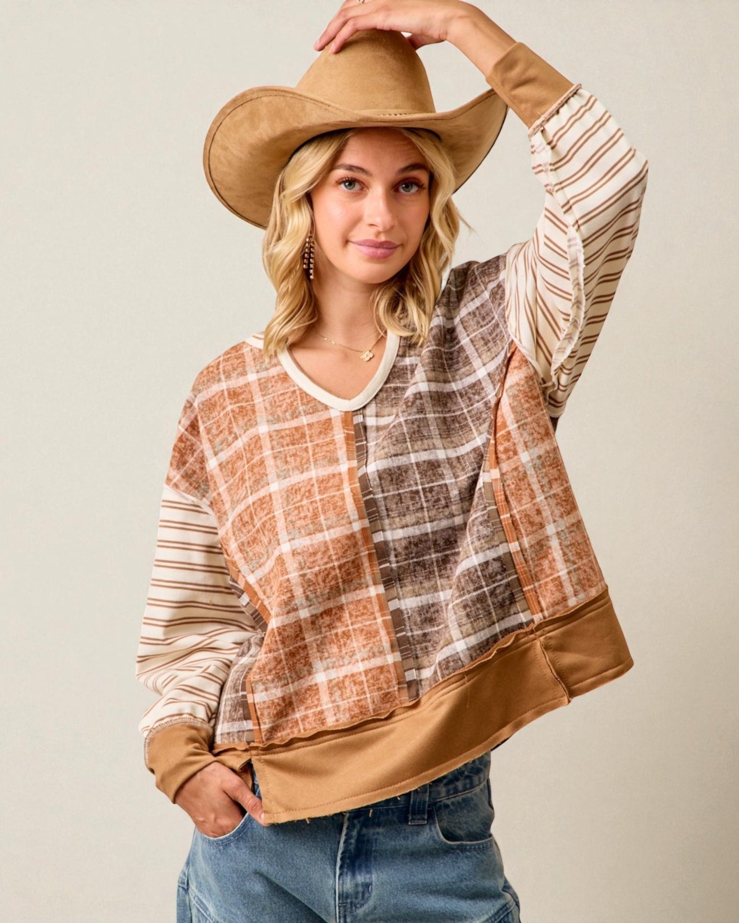 Woman wearing a plaid shirt over a brown top with a wide-brimmed hat on a plain background