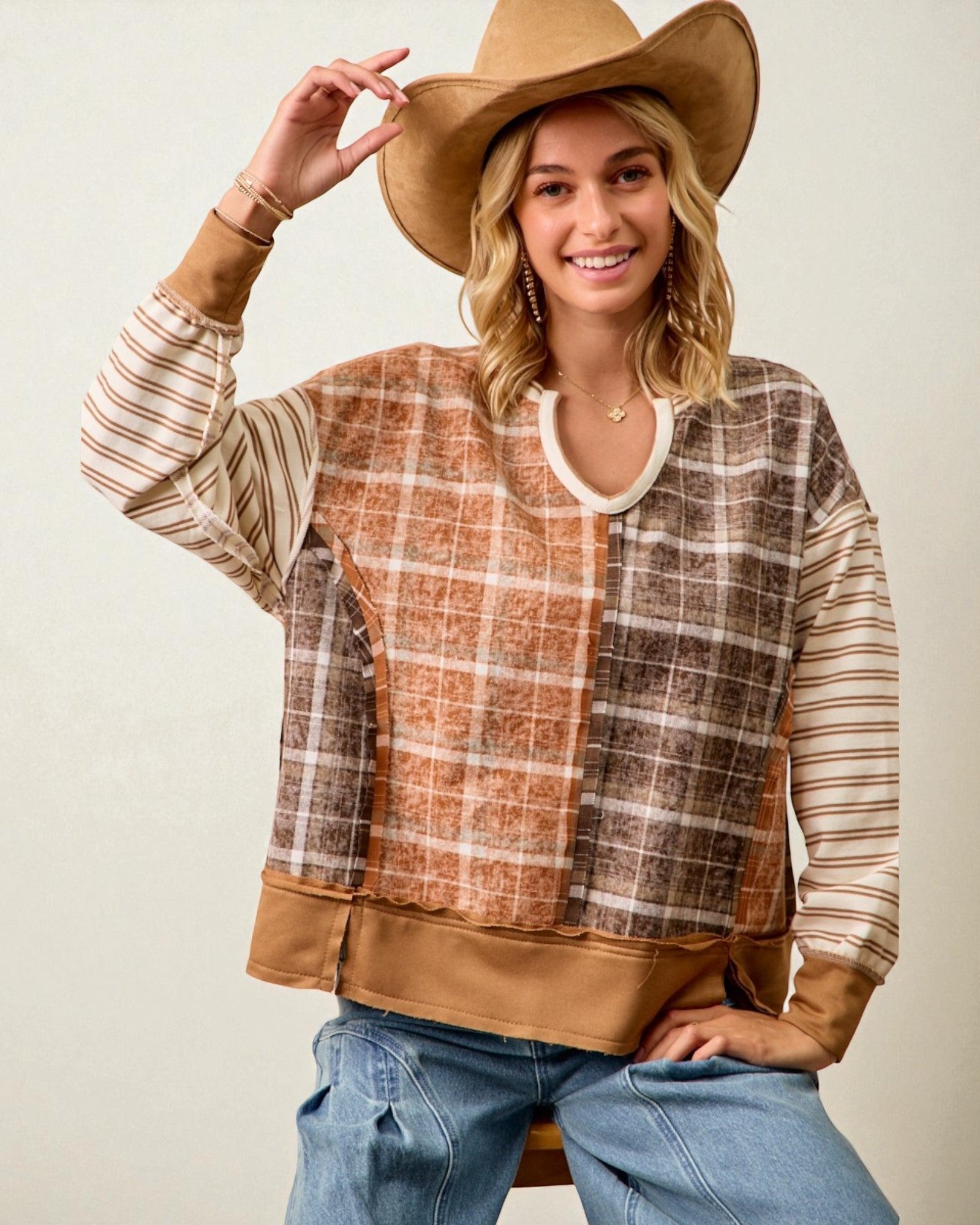 Woman wearing a plaid shirt with brown accents and a wide-brimmed hat on a plain background