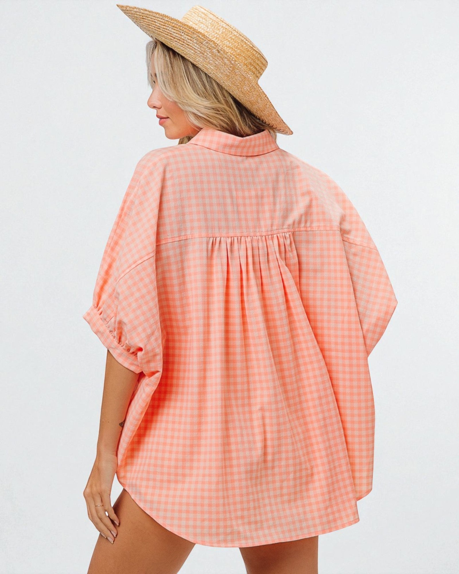 Woman wearing a peach checkered dress and straw hat on a light gray background