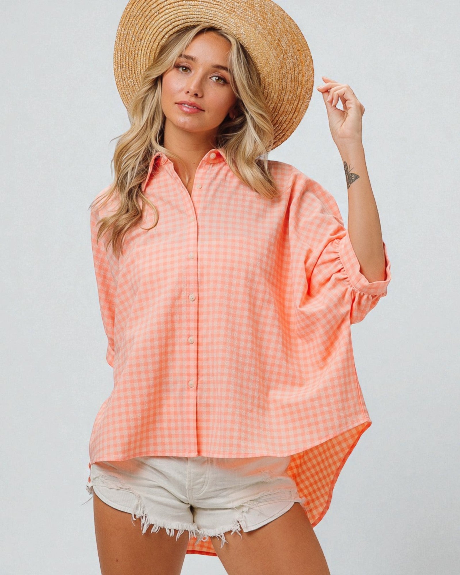Woman wearing a peach checkered shirt and straw hat on a plain background