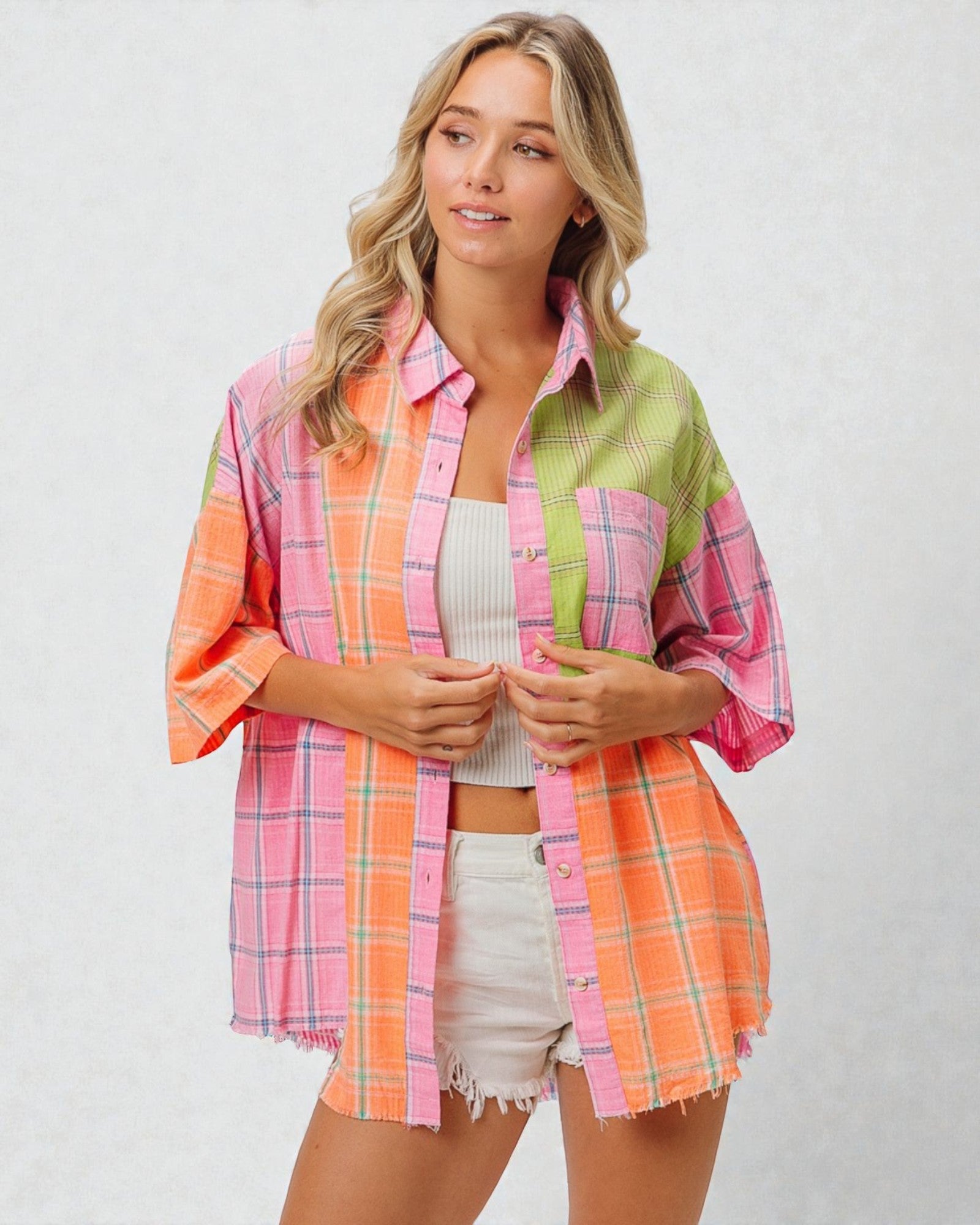 Woman wearing a colorful plaid shirt over a white top and shorts on a light gray background