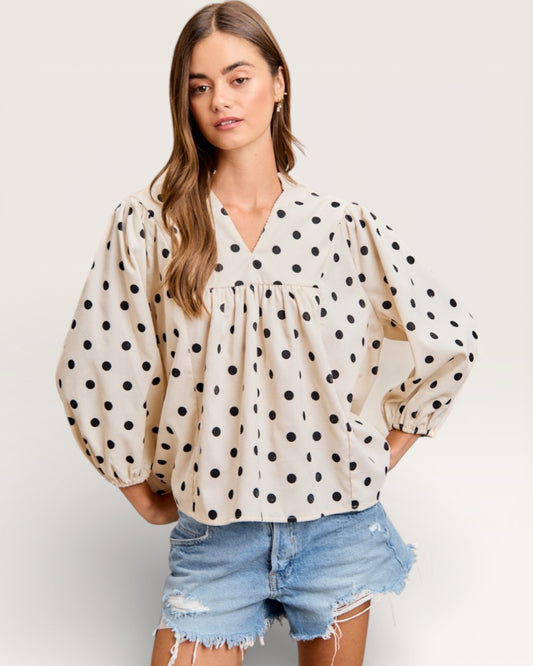 Woman wearing a polka dot blouse and denim shorts on a plain background