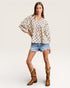 Woman wearing a polka dot blouse, denim shorts, and brown cowboy boots on a white background