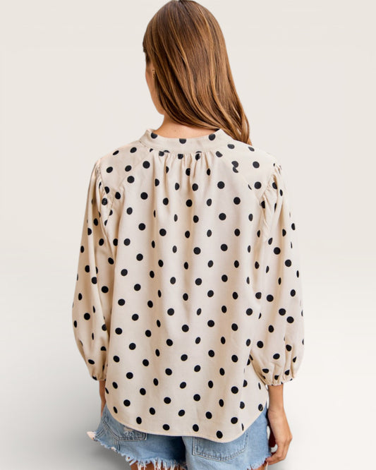 Woman wearing a beige blouse with black polka dots on a plain background