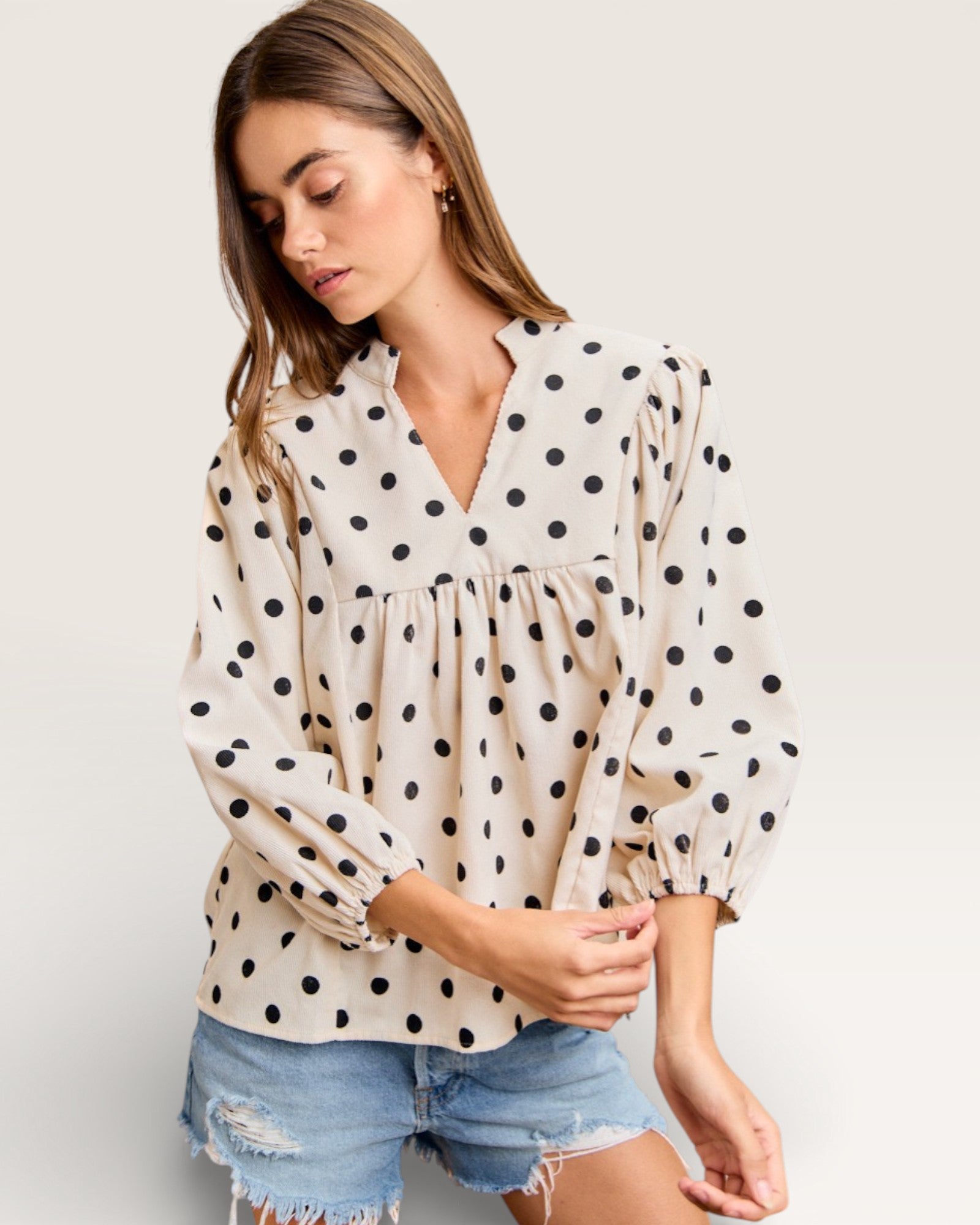 Woman wearing a polka dot blouse and denim shorts on a plain background