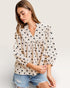 Woman wearing a polka dot blouse and denim shorts on a plain background