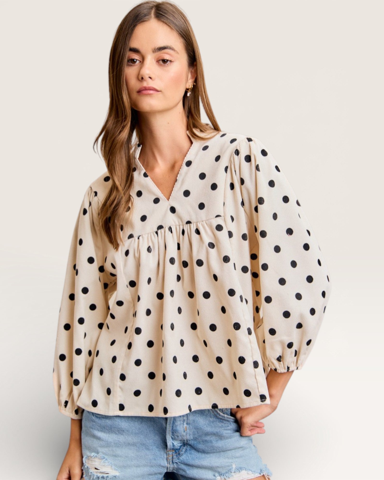 Woman wearing a polka dot blouse with balloon sleeves on a plain background