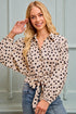 Woman wearing a beige blouse with black polka dots and blue jeans against a light-colored wall.