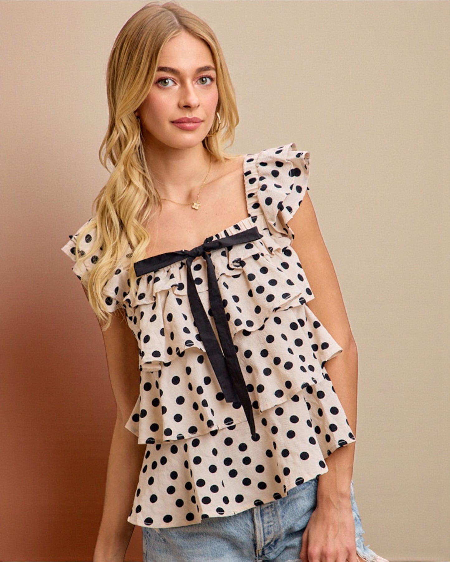 Woman wearing a polka dot top with ruffled layers on a beige background