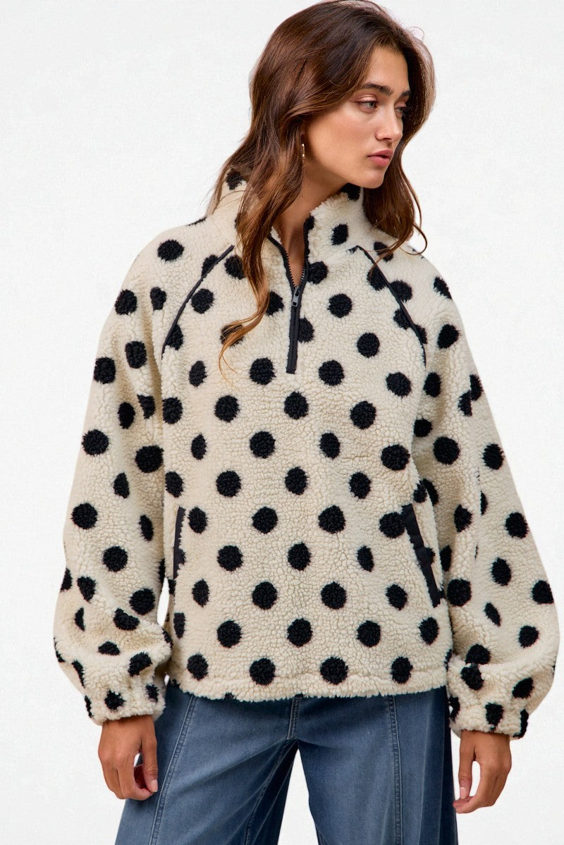 Woman wearing a cream fleece pullover with black polka dots on a white background