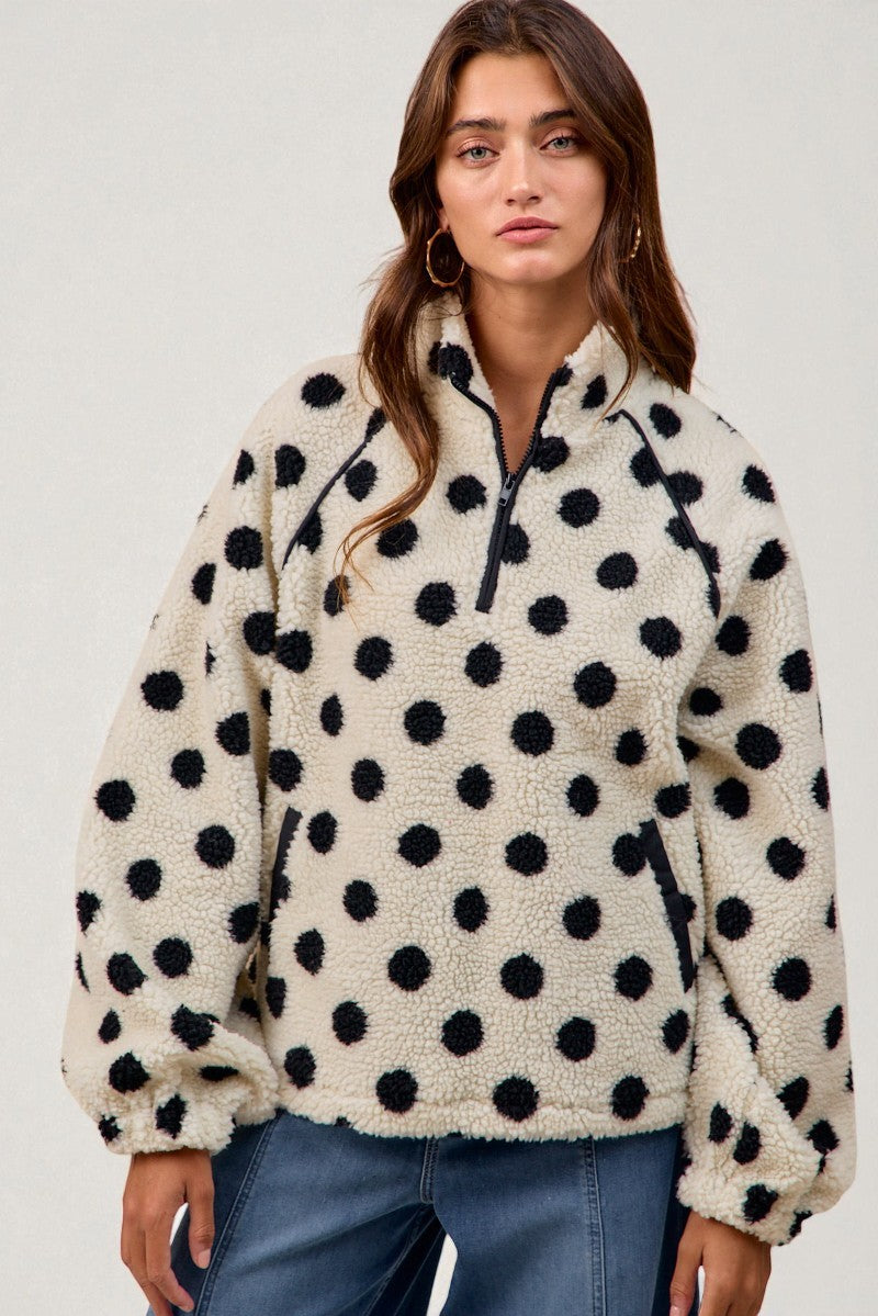Woman wearing a cream-colored fleece pullover with black polka dots against a plain background