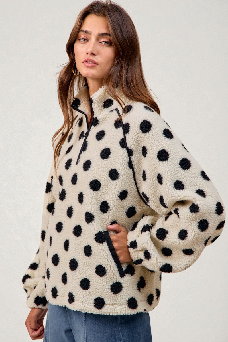 Woman wearing a cream-colored fleece pullover with black polka dots on a white background