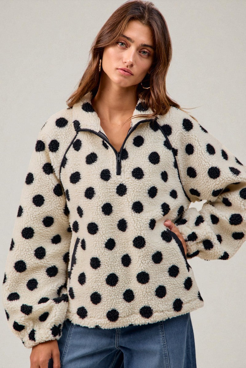 Woman wearing a cream fleece pullover with black polka dots against a plain background