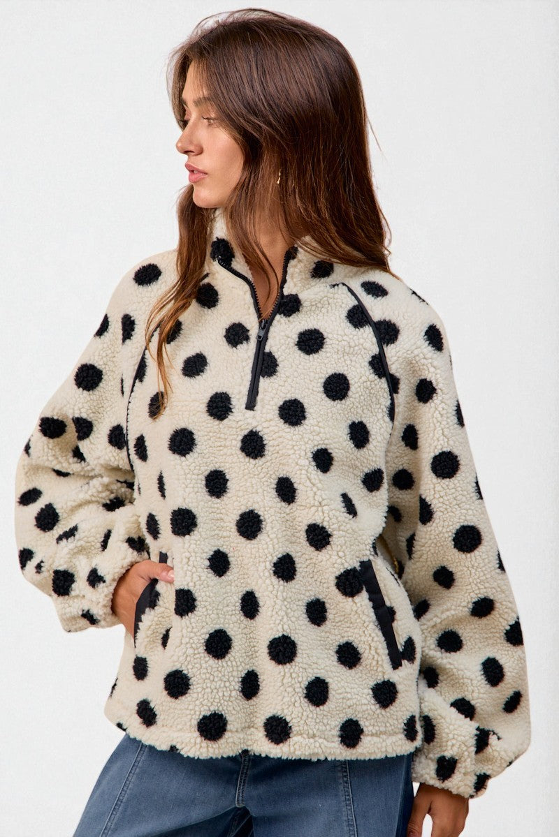 Woman wearing a cream-colored fleece pullover with black polka dots on a white background