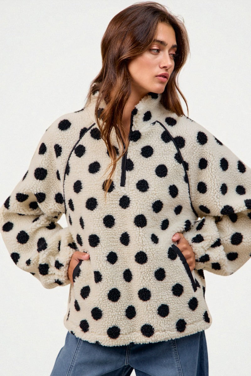 Woman wearing a cream-colored fleece jacket with black polka dots on a plain background