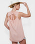 Woman wearing a pink sleeveless top with a bow detail on the back, white hat, and denim shorts against a white background.