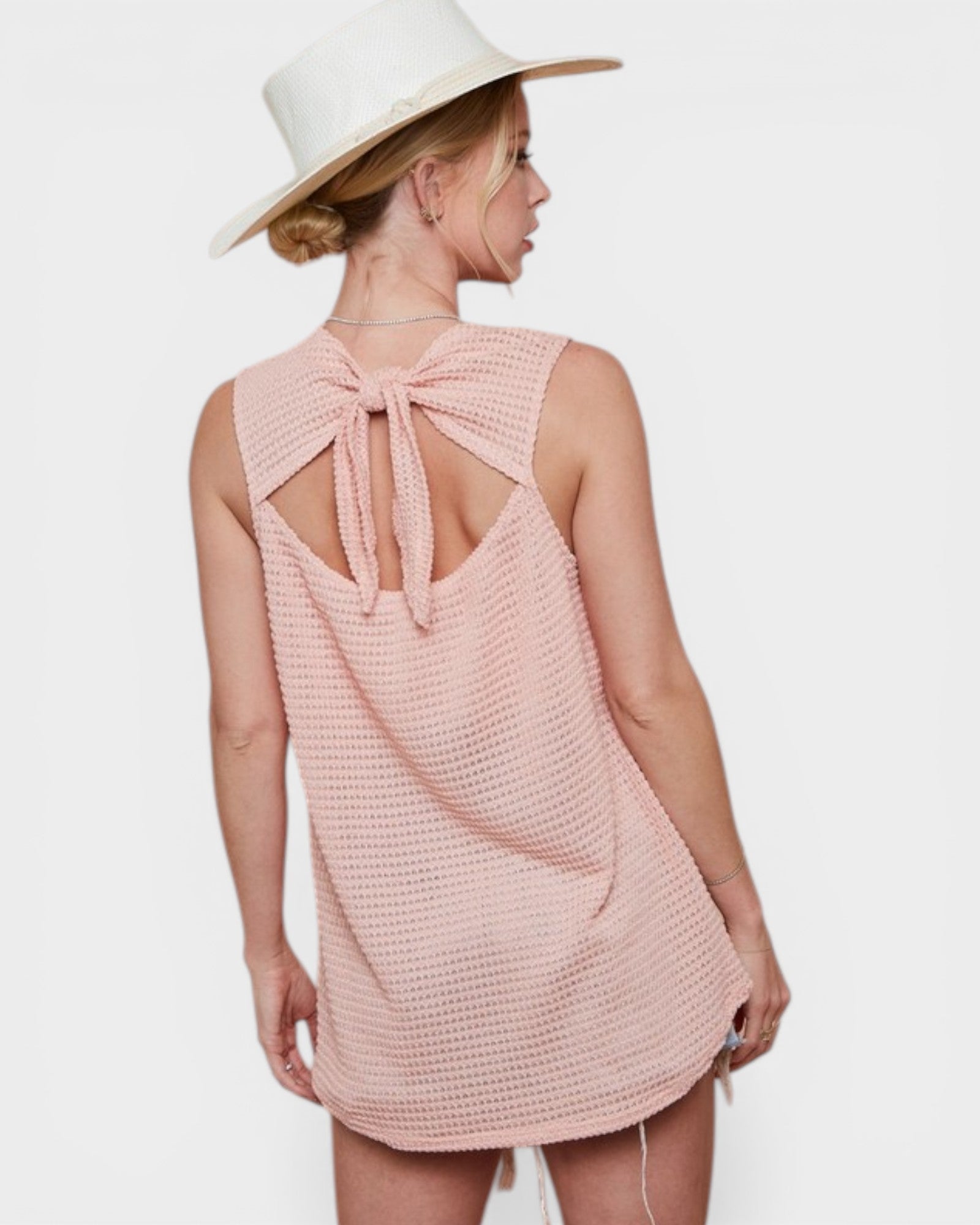 Woman wearing a pink sleeveless dress with a bow detail on a white background
