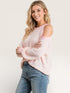 Woman wearing a pink cold-shoulder sweater and blue jeans on a white background