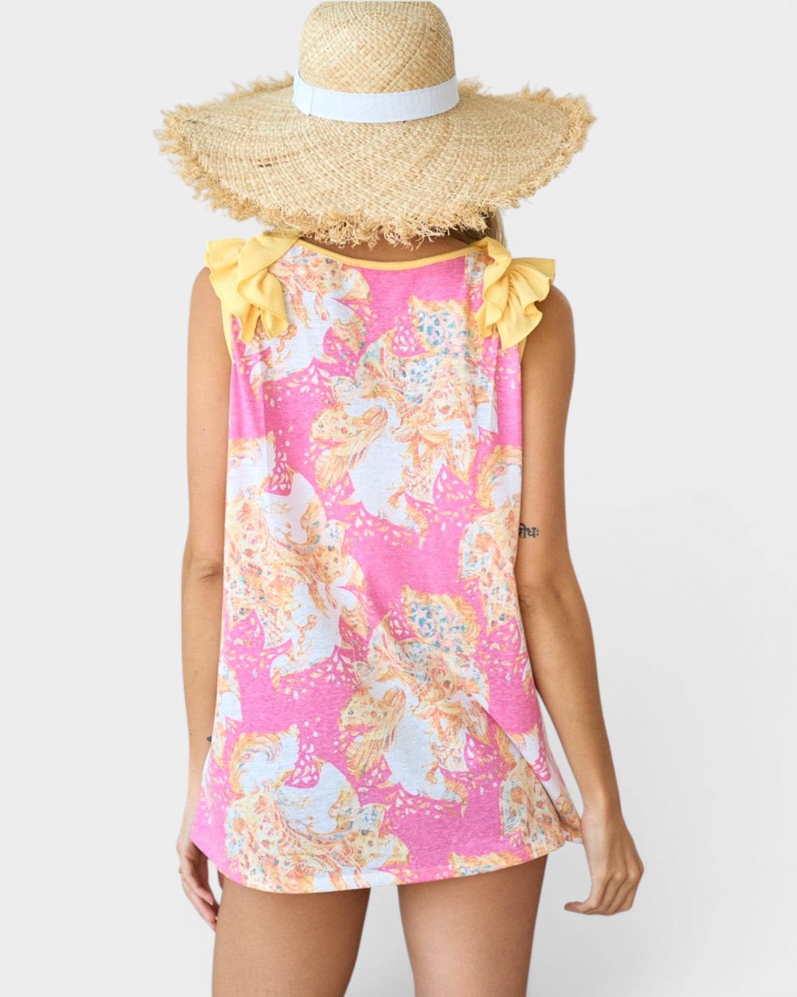 Woman wearing a pink floral top with yellow ruffled sleeves and a wide-brimmed straw hat on a white background