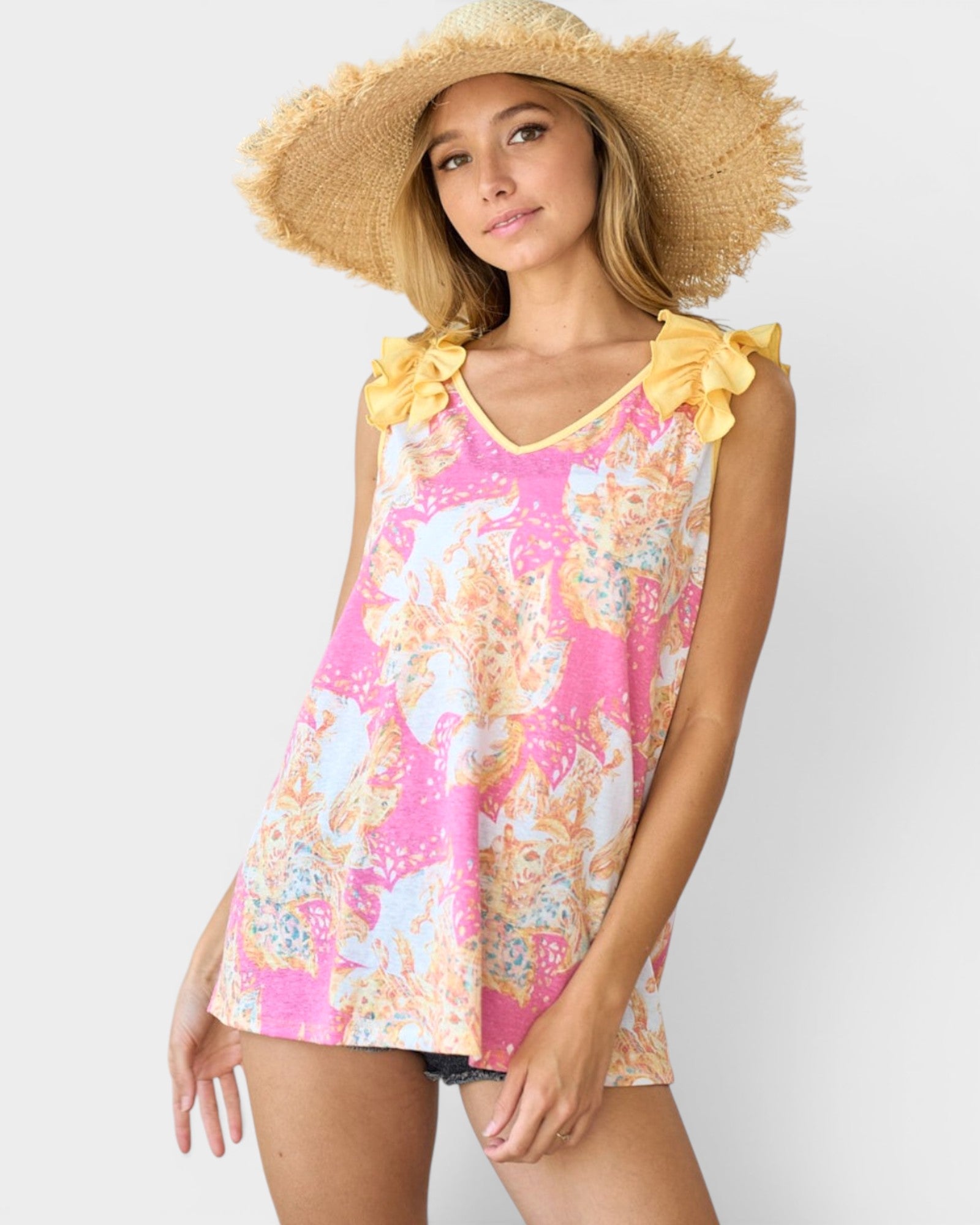 Woman wearing a floral top with yellow ruffled sleeves and a straw hat on a white background