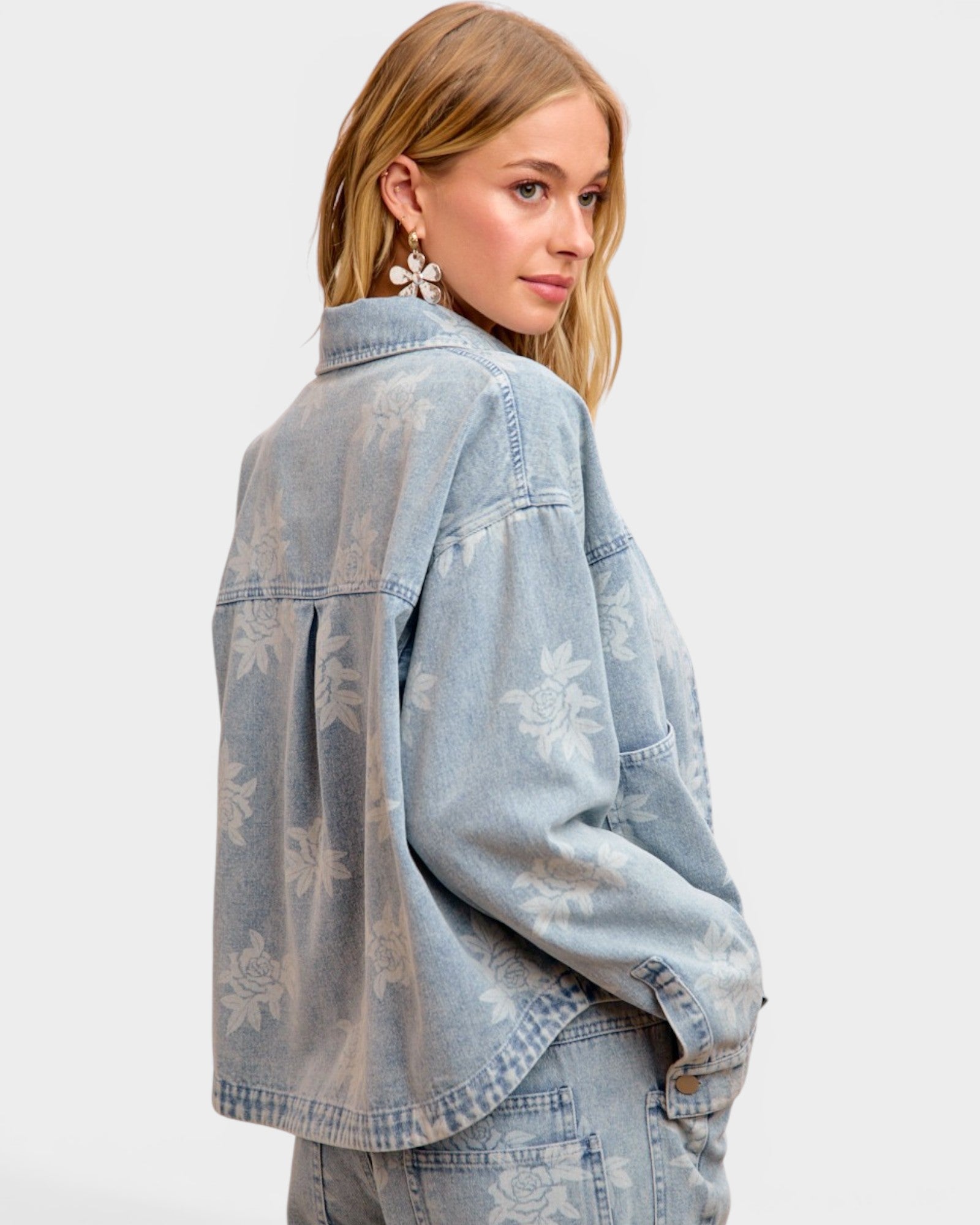 Woman wearing a light blue denim jacket with floral patterns on a white background
