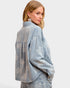 Woman wearing a light blue denim jacket with floral patterns on a white background