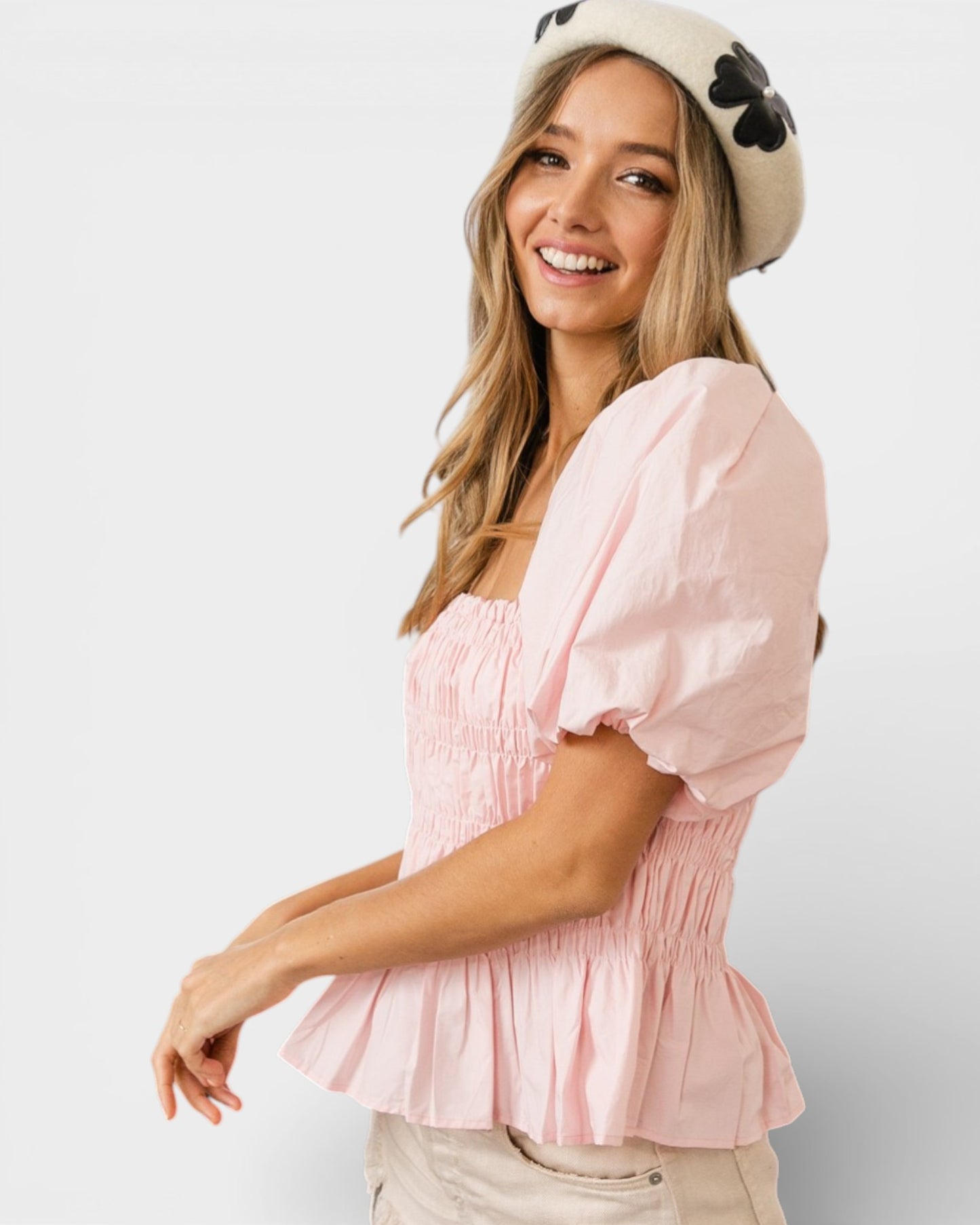 Woman wearing a pink blouse and a white hat with black polka dots on a light gray background