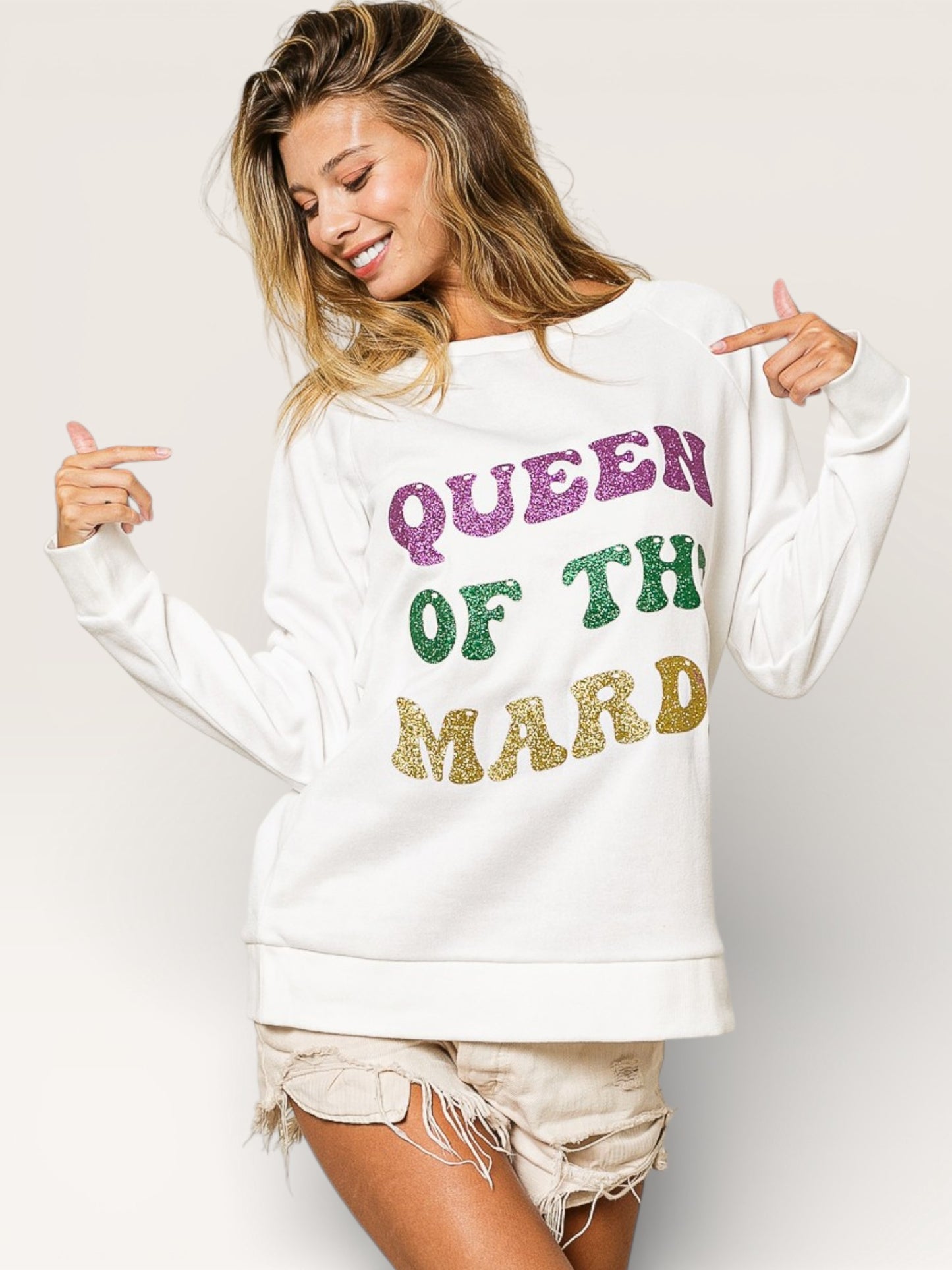 Woman wearing a white sweatshirt with colorful text 'QUEEN OF THE MARD' on a plain background