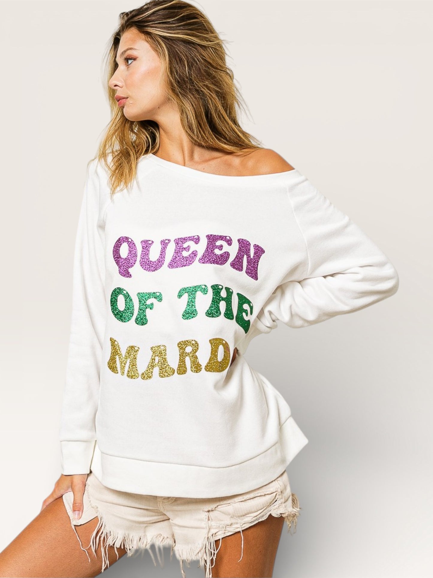 Woman wearing a white sweatshirt with colorful text 'QUEEN OF THE MARDI' on a plain background