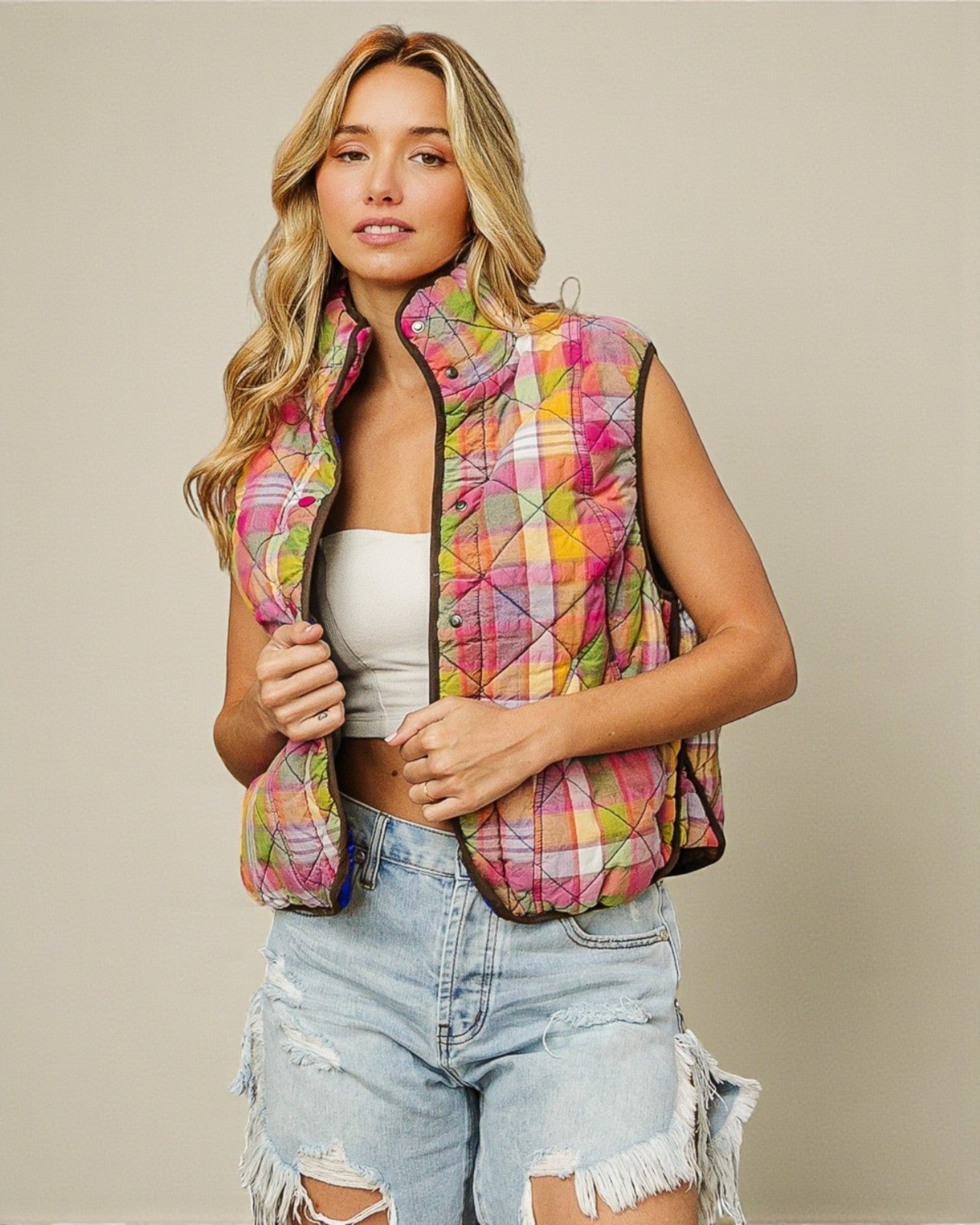Woman wearing a colorful quilted vest over a white top and denim shorts on a beige background