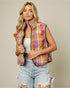 Woman wearing a colorful quilted vest over a white top and denim shorts on a beige background