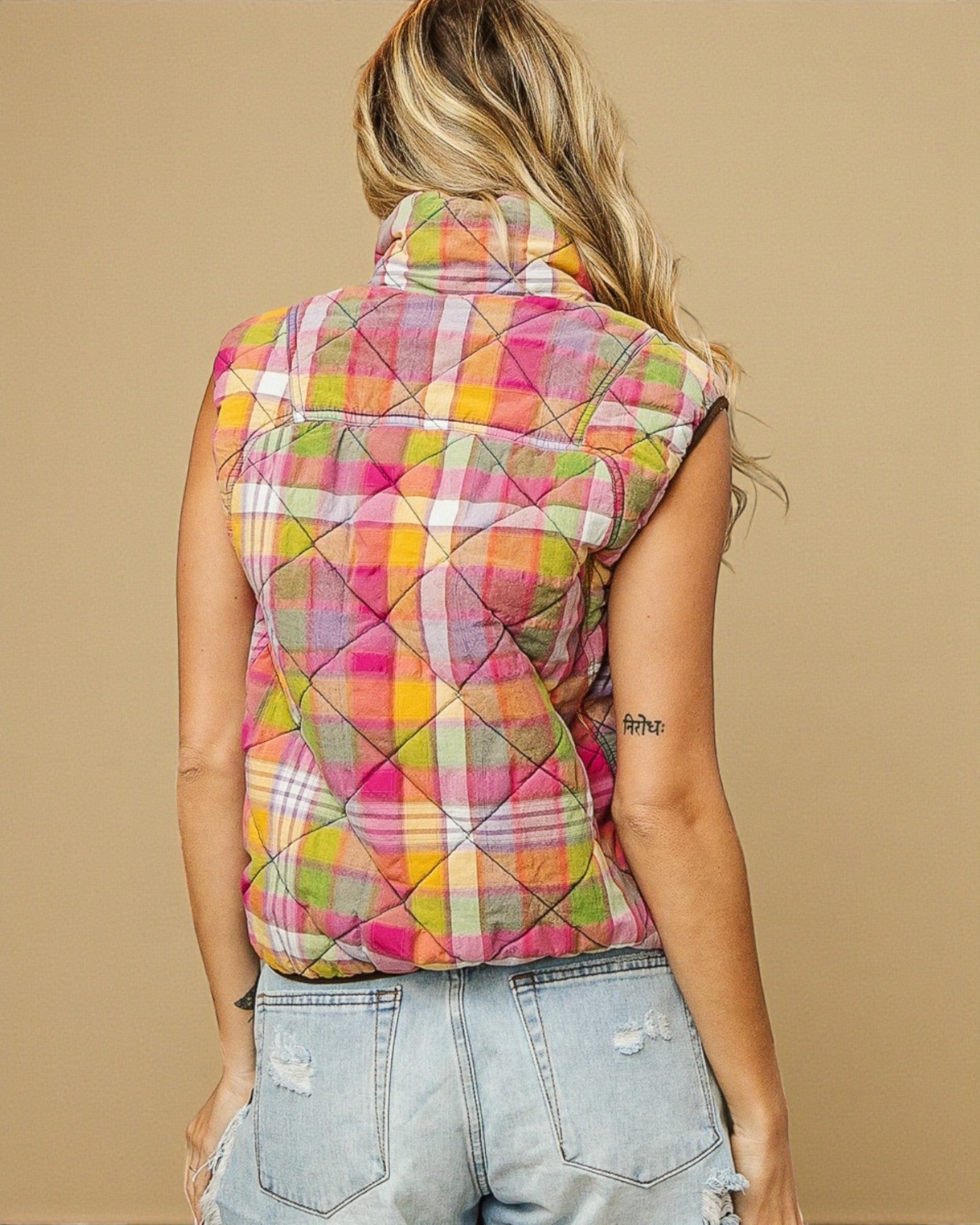 Person wearing a colorful quilted vest against a beige background