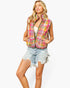 A woman modeling a sleeveless quilted puffer vest with a vibrant multicolor plaid pattern in pink, yellow, orange, and green, paired with light-wash denim shorts against a plain white background.